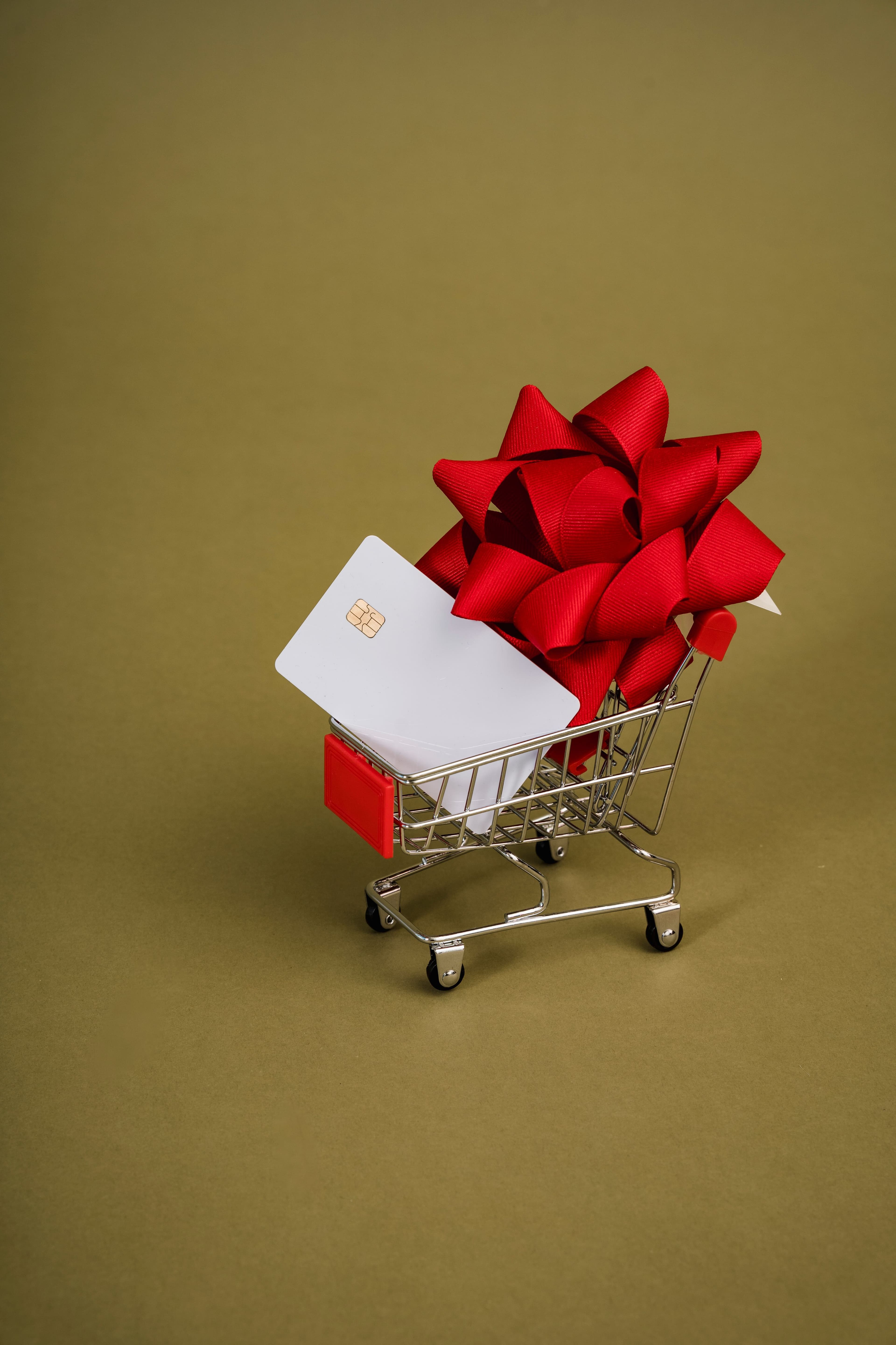 A miniature shopping trolley holding a gift card and a red gift bow