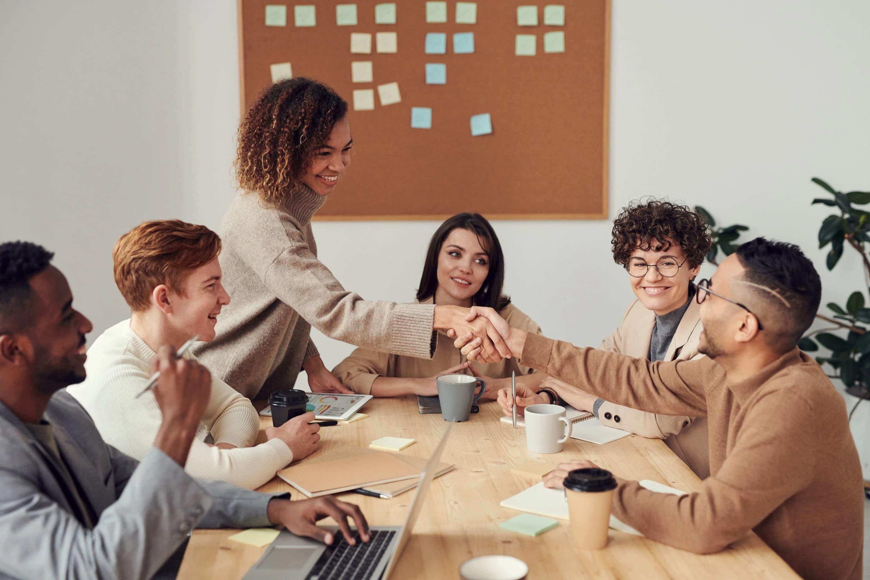 A group of six colleagues sharing ideas and shaking hands around an office table